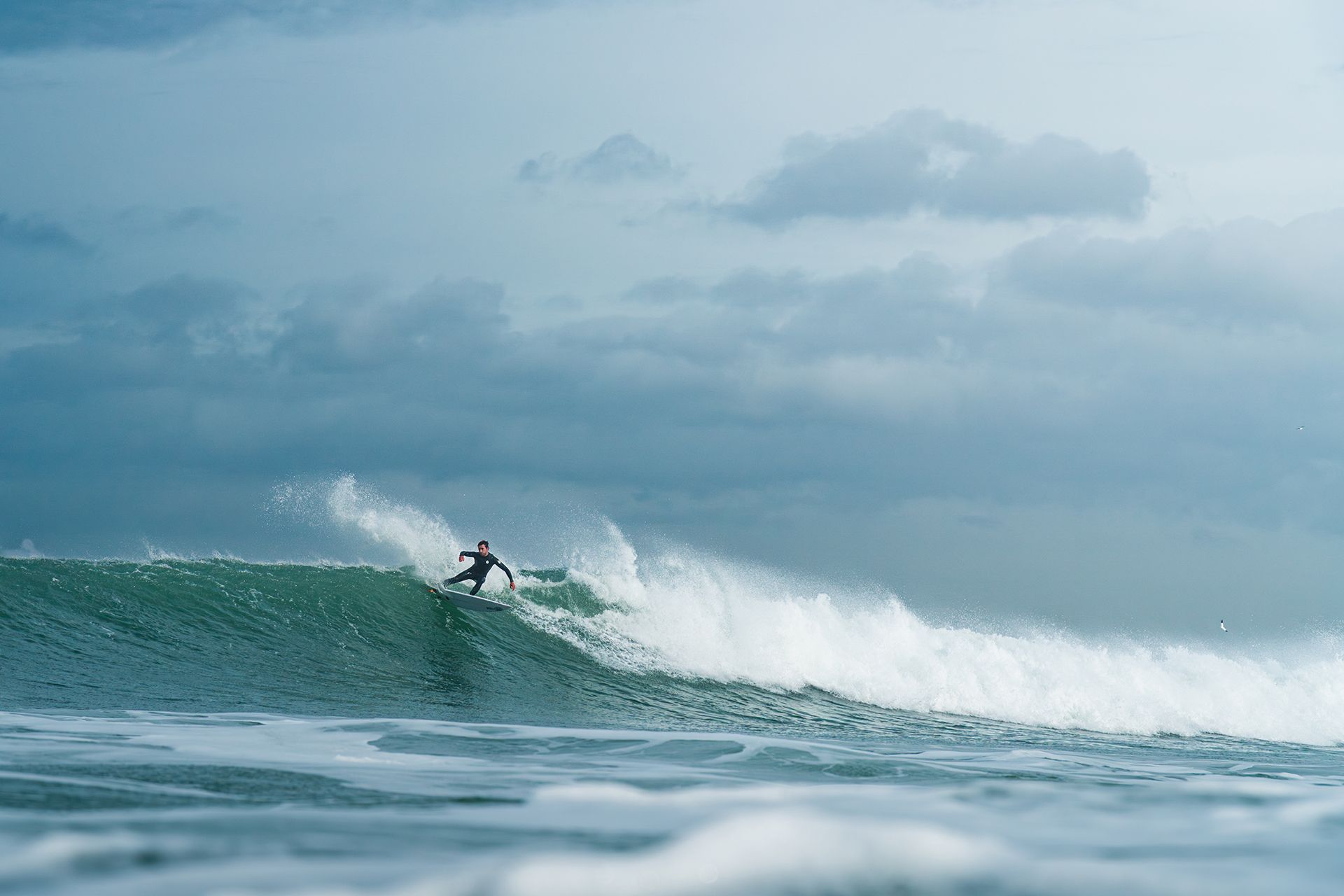 Surfer driving off the bottom in a burst of spray on an overcast Atlantic day.