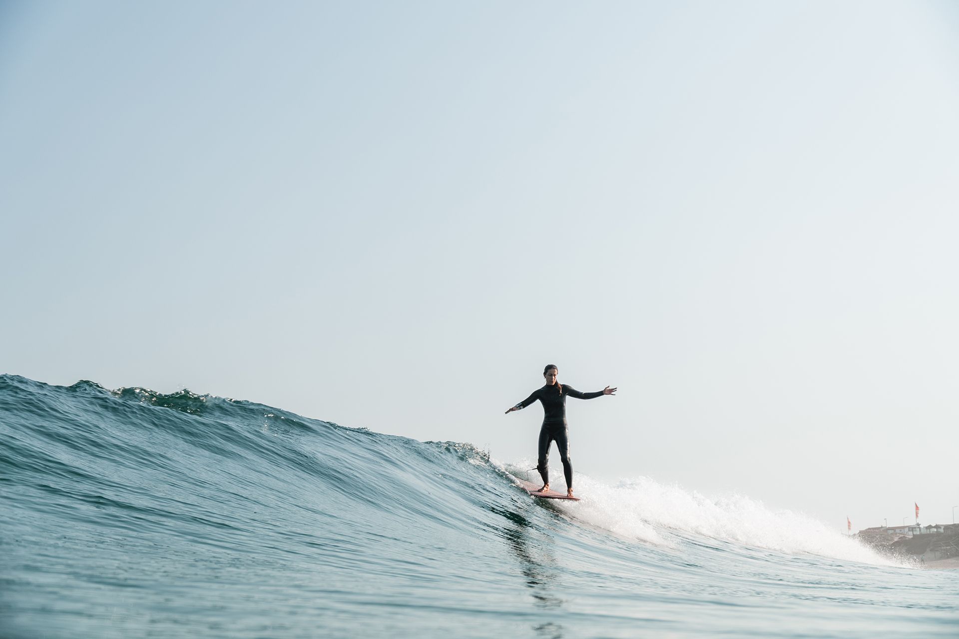 Lone longboarder cross-stepping on a clean waist-high wave under a pale morning sky.