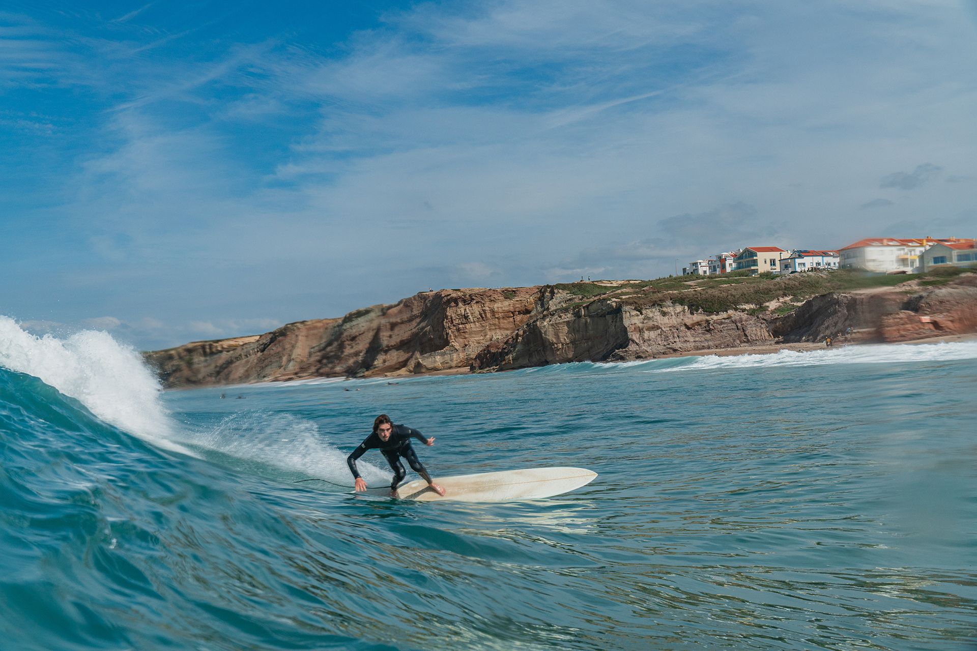 Longboarder noseriding a peeling wave with the cliffs and houses of Baleal behind.