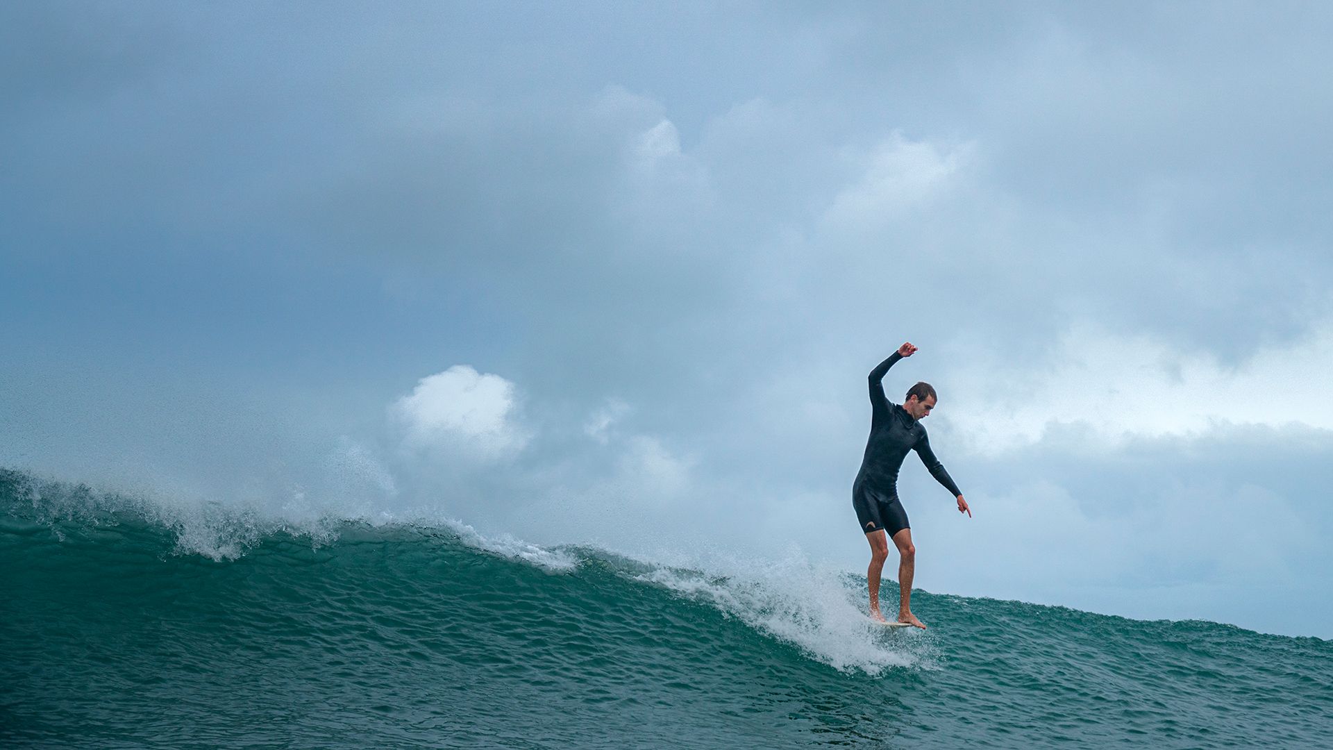 Surfer setting his line on the drop of a grey, glassy shoulder-high wave.