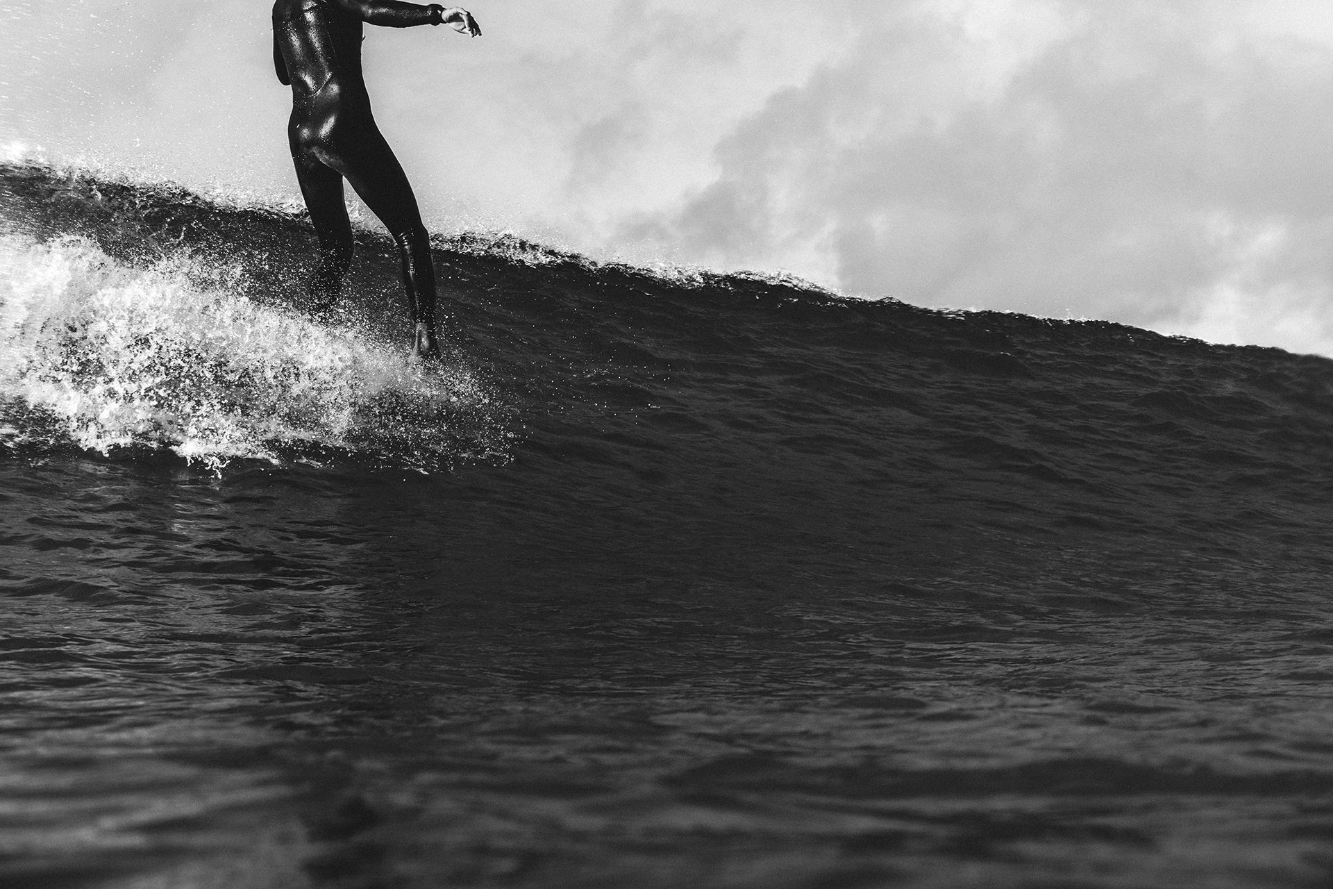 Black and white close crop of a surfer walking the nose, lit by bright spray.