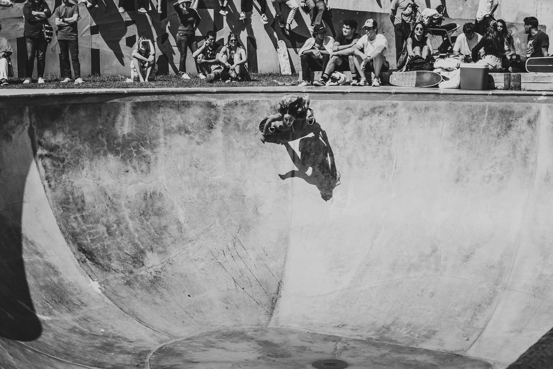 Black and white shot of a skater flying across a concrete bowl above a crowd of onlookers.