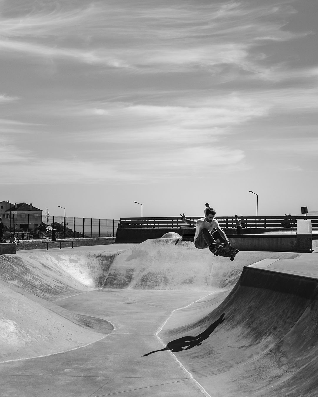 Skater catching air over the spine of a concrete park, sea and rooftops on the horizon.
