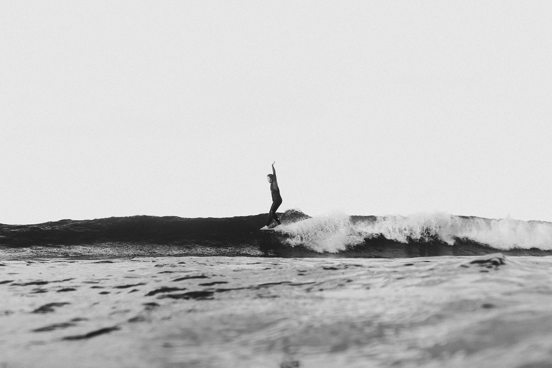 Surfer riding high on the shoulder of a clean waist-high wave with one arm raised.